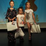 trzy dziewczynki z torbami stoją na scenie