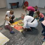 dzieci i dorośli malują na ziemi kolorowymi farbami