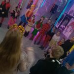 dzieci w przebraniach stoją w kółku nad nimi zwisa kolorowa bibułka i balony