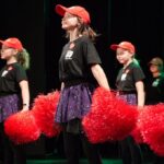 dziewczyny w czerwonych czapkach i pomponami tańczą na scenie