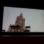 slajd wyświetlany na ekranie na którym jest pałać kultury w Warszawie na scenie stoi stolik i dwa krzesła