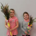 dwie dziewczynki stoją trzymając w rączkach palmy wielkanocne