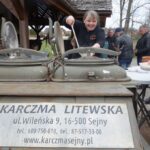 karczma litewska u. wileńska 9, 16-500 Sejny uśmiechnięta kobieta wielką chochlą z kuchni polowej nalewa uśmiechniętej kobiecie zupę z tyłu za nimi grupa mężczyzn