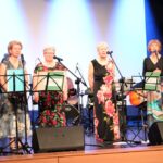 pięć kobiet w sukniach w kwiaty śpiewa na scenie