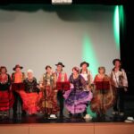 5 kobiet w cygańskich sukniach i 5 mężczyzn w cygańskich strojach śpiewaja na scenie