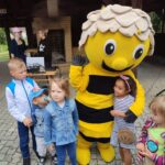 czwórka dzieci stoi wokół dużej maskotki pszczółki