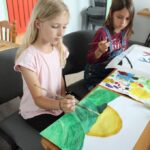 dwie dziewczynki siedzą przy stole malują farbkami
