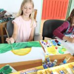 dwie dziewczynki siedza przy stole malują farbkami