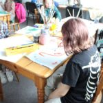 grupa dzieci siedząca przy stołach malująca farbkami