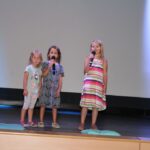 trzy dziewczynki stoją na scenie z mikrofonem