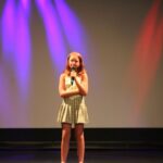 dziewczynka stoi na scenie z mikrofonem