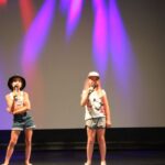 dwie dziewczynki stoi na scenie z mikrofonem