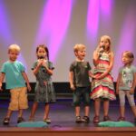 trzy dziewczynki i dwóch chłopców stoją na scenie i śpiewają