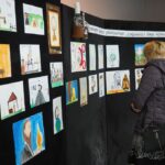 kolorowe prace plastyczne dzieci na czarnej zastawce kobieta ogląda prace