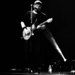 czarno- białe zdjęcie przedstawiające mężczyznę stojącego przed mikrofonem z gitara.