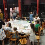 grupa dzieci i dorosłych przy siedzą przy kolorowym stole