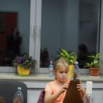 dziewczynka siedzi przy stole przykleja krepinę do butelki
