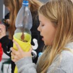 dziewczynka trzyma w rękach butelkę oklejoną żółtą bibułą