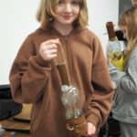 dziewczynka w brązowej bluzie trzyma wykonaną przez siebie lampę naftową