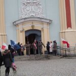 grupa osób przed wejściem do kościoła i flagi biało - czerwone