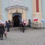 grupa ludzi przed wejściem do kościoła i flagi