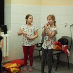 dwie dziewczynki jedna z nich trzyma mikrofon i spiewa