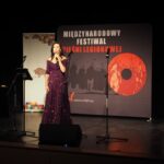 kobieta stoi na scenie i śpiewa, za nim napis Międzynarodowy Festiwal Pieśni Legionowej
