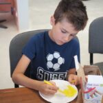 chłopiec siedzi malując żółtym mazakiem papierowy talerzyk