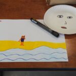 kartka z kolorowymi rysunkami w rogu papierowy talerzyk z narysowaną buzią