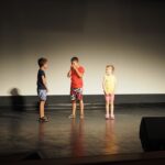 dwóch chłopców i dziewczynka stoją na scenie