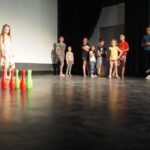 dzieci stoją w rzędzie na scenie patrzą na kolorowe kręgle