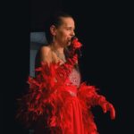 kobieta w czerwonej sukni z piórami z mikrofonem na scenie