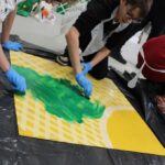 2 chłopców maluje zieloną farbą żółtą planszę